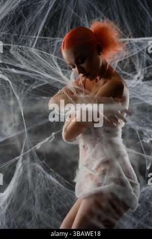Red-haired woman caught in an intricate net trap surrounded by webs Stock Photo