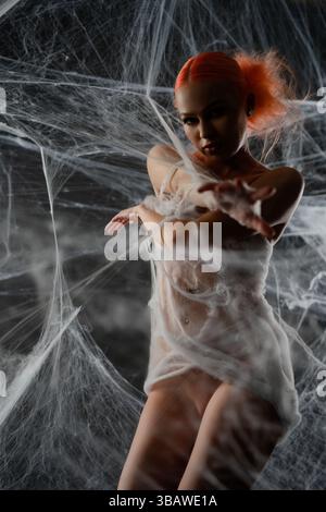 Red-haired woman is caught in a net trap surrounded by webbing at dusk Stock Photo