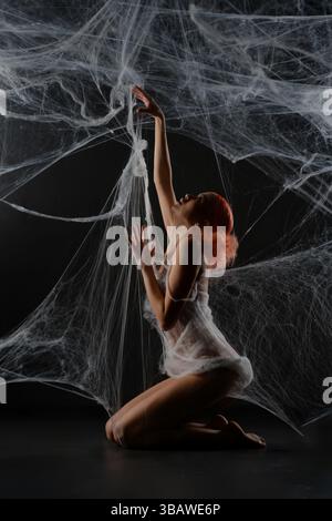 Red-haired woman entangled in a net trap resembling a spider web Stock Photo