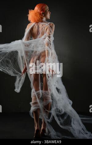 Red-haired woman caught in a delicate net trap in an artistic setting Stock Photo