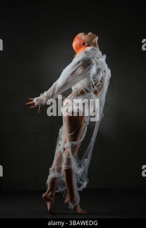 Red-haired woman entangled in a delicate web under soft lighting Stock Photo