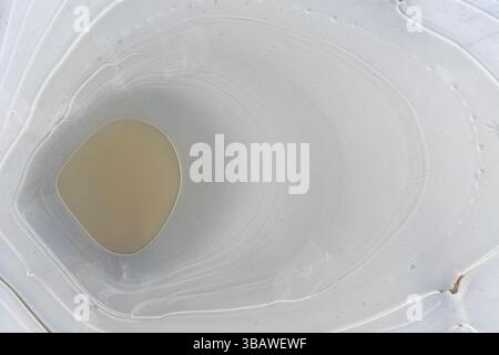 Overhead view of a frozen puddle with abstract ice formations and trapped air bubbles. Natural winter texture ideal for seasonal or design use. Stock Photo