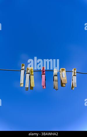 Brightly colored plastic clothespins hanging on a wire with clear blue sky in the background. Stock Photo