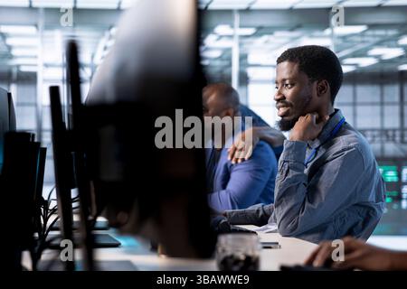 Smiling engineer in data center next to colleagues updating systems to keeps performance up and protect servers from software vulnerabilities. Coworkers looking for errors causing servers to slow down Stock Photo