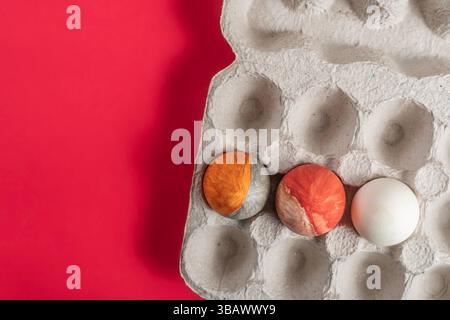 Hand painted Easter eggs with vibrant colors placed in a cardboard box on a red background. Stock Photo