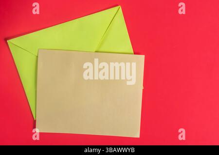 A green envelope and brown card set against a vibrant red background. Perfect for communication, creativity, or celebration themes. Stock Photo