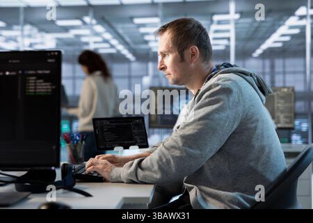 Focused man working in server farm capable of processing vast amounts of data. IT programmer at PC desk typing on keyboard, updating servers controlling network resources Stock Photo