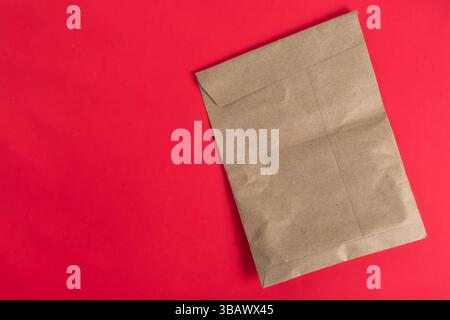 A brown paper bag placed on a vibrant red background symbolizing eco-friendly ideas and minimalism. Stock Photo