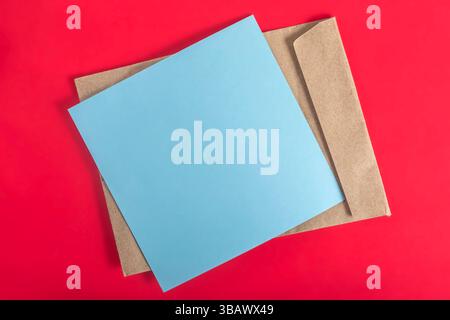 The blue paper and brown envelope are beautifully arranged on a vibrant red surface, showcasing a minimalist design. Stock Photo