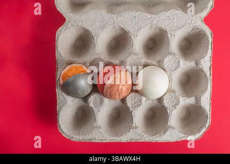 An overhead view of three colorful eggs placed in an open cardboard box set on a bright red surface provides a festive and creative display perfect fo Stock Photo