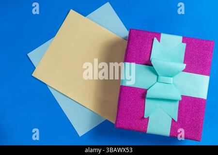 A bright purple gift box decorated with a teal bow embedded in colorful sheets on a blue surface. For celebration, gift giving and festive occasions, Stock Photo