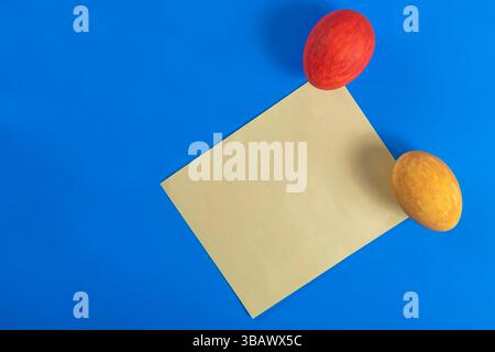 Easter themed arrangement of yellow paper and two colorful eggs placed on a dark blue background. Perfect for seasonal design. Stock Photo