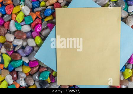 A composite consisting of vibrant, multi colored pebbles and plain brown and blue sheets of paper, perfect for promotional materials. Stock Photo