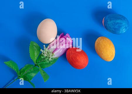 A vibrant Easter themed composition with decorative eggs and a pink artificial rose on a blue background. Stock Photo