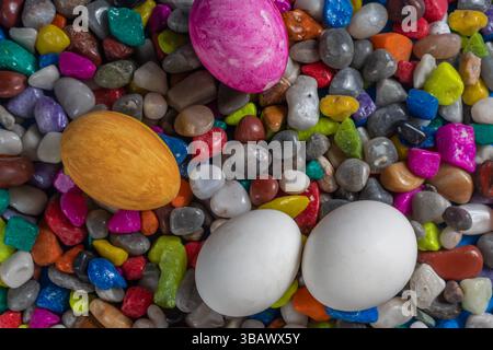 Colored Easter eggs, including white, pink, and yellow, lie a top a bed of multicolored pebbles. perfect background for spring celebrations, and festi Stock Photo