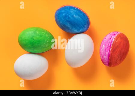Top view of vibrant Easter eggs resting on an orange surface display artistic colorful painted patterns. Stock Photo