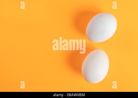 Two white eggs placed on an orange background create a colorful and minimalist composition, perfect for art or kitchen related themes. Stock Photo