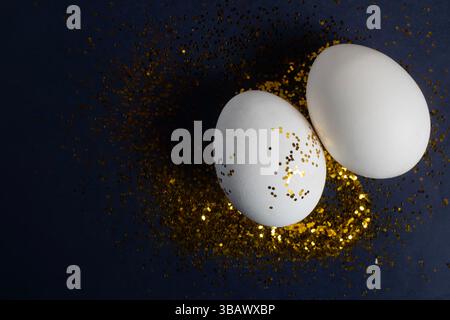White eggs decorated with gold glitter are set on a dark surface, evoking the elegance of Easter. Stock Photo