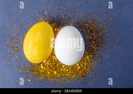 Decorative yellow and white eggs on a blue background, surrounded by shimmering gold glitter, symbolize creativity and celebration. Stock Photo