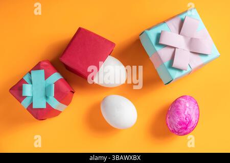 Decorative Easter gifts and colorful eggs are arranged on a vibrant orange background, evoking a festive and joyful atmosphere. Stock Photo