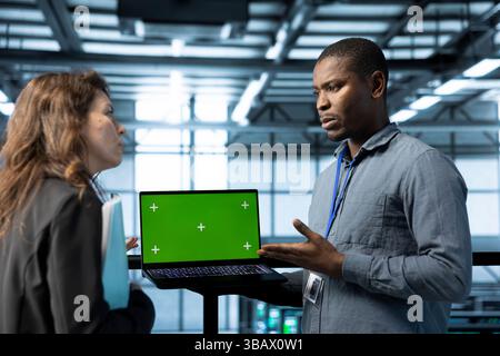 Engineer in data center using chroma key laptop, refining server virtualization strategies. Employees using isolated screen notebook to configure server cluster nodes, maintaining efficient workflows Stock Photo
