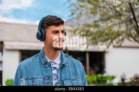 A young happy man with headphones is walking the city street. Stock Photo