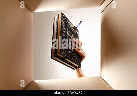 A woman hand putting books in a cardboard box. View from the inside. Stock Photo
