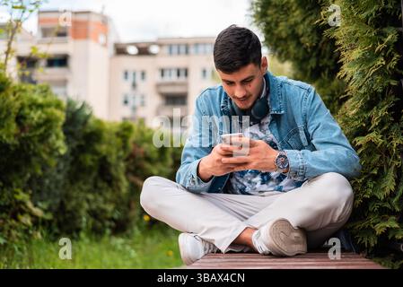 A young happy man using a mobile phone in the city park. Stock Photo