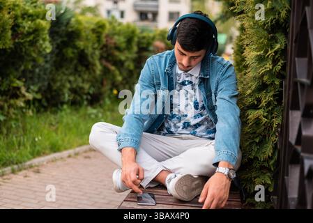 A young man with headphones using a mobile phone outside. Stock Photo