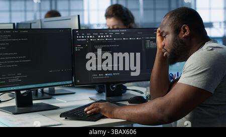 Overworked engineer falling asleep while typing on computer in server hub, monitoring data center energy consumption. Tired technician struggling to stay awake while inspecting rackmounts, camera A Stock Photo