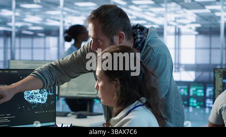 IT team members programming scripts on computer, employing AI machine learning. Software developer and coworker manipulating lines of code for artificial intelligence applications, camera A Stock Photo