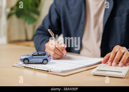 A man signs car insurance documents, calculating costs with a loan calculator. Writing his signature Stock Photo