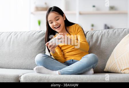 Emotional fmale kid having fun at home, using smartphone Stock Photo