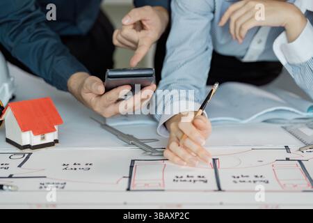 Engineers reviewing architectural plans and calculations with tools and a model house. Stock Photo