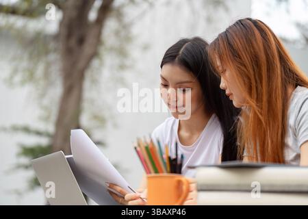 Diverse female students focused on study materials with laptop and stationery. Stock Photo
