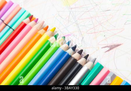 Multi-colored pencils lie on white paper drawn with multi-colored curved lines. Stock Photo