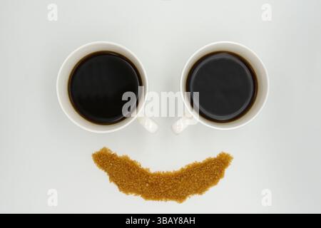 a two porcelain coffee cups with Americano and sprinkled sugar in the form of a smiley face on a white background Stock Photo