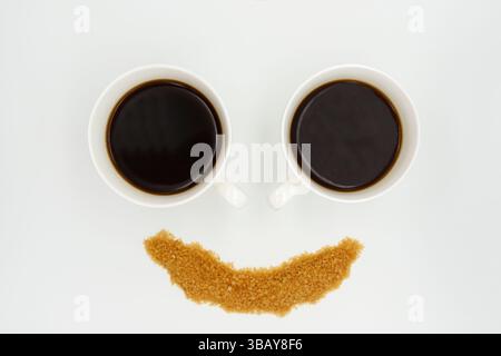a two porcelain coffee cups with Americano and sprinkled sugar in the form of a smiley face on a white background Stock Photo