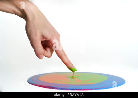 a human hand with a finger touching a circle of colors and mixing them Stock Photo