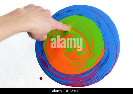 a human hand with a finger touching a circle of colors and mixing them Stock Photo