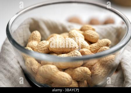 Roasted peanuts in glass bowl on crumpled cloth napkin close up Stock Photo