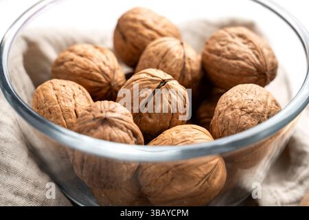 Whole raw walnuts with nutshells in glass bowl. Close-up. Stock Photo