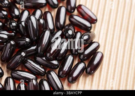 Dark capsules of omega 3 supplement on corrugated cardboard packaging sheet. Nutritional black red softgels in brown paper box. Macro shot Stock Photo