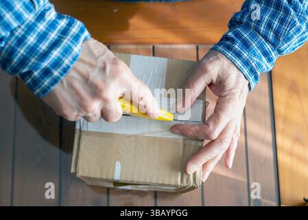 A person unsealing a cardboard box using a yellow utility knife, depicting careful handling and packaging. This activity represents shipping, delivery Stock Photo