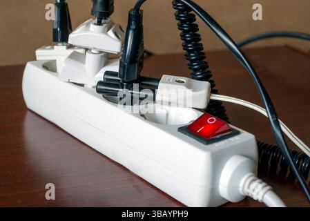 A close-up of an overloaded electrical power strip with multiple plugs and cables connected, highlighting precautions for proper appliance use at home Stock Photo