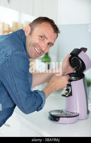 man repairing coffee machine with screwdriver in kitchen Stock Photo