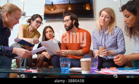 Multi-Cultural Business Team Sitting On Sofa In Office Reviewing Documents Stock Photo