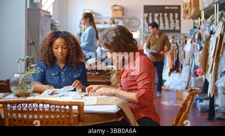 Two Young Women Working In Fashion Design Studio Meeting And Discussing Fabric Samples Stock Photo