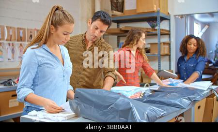 Team Using Digital Tablet Working In Distribution Warehouse Packing Clothes For Customer Delivery Stock Photo