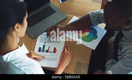Male And Female Business Colleagues With Laptop Sitting At Desk In Office Discussing Documents Stock Photo